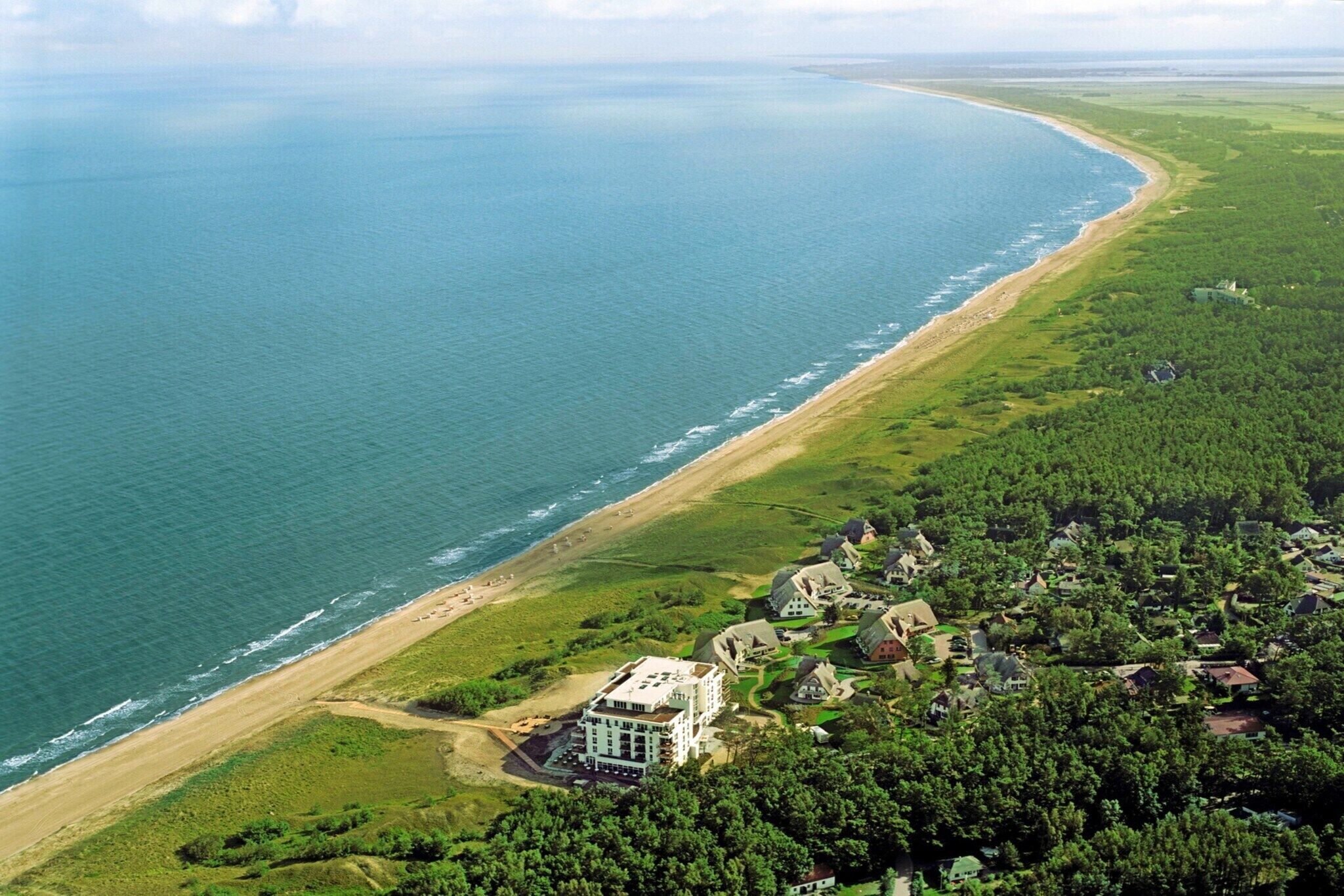 Eine Luftaufnahme einer Küstenregion mit Strand, einem großen, mehrstöckigen Gebäude und umgebender Vegetation.