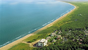 Eine Luftaufnahme einer Küstenregion mit Strand, einem großen, mehrstöckigen Gebäude und umgebender Vegetation.