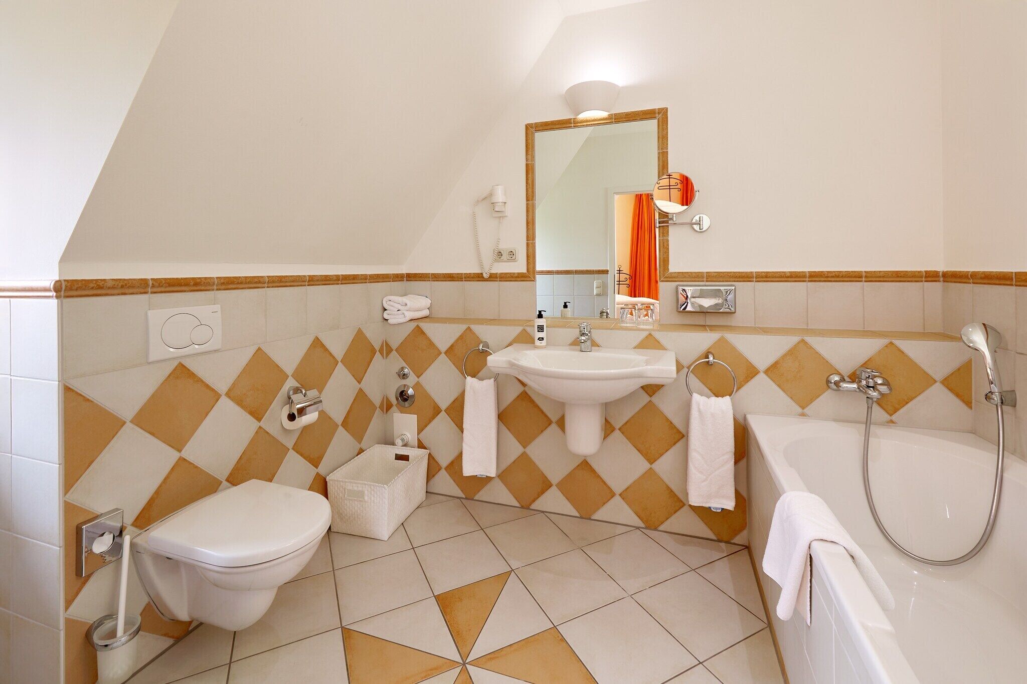 Une salle de bain comprenant des toilettes, un lavabo et une baignoire, avec un motif géométrique sur les murs et le sol.