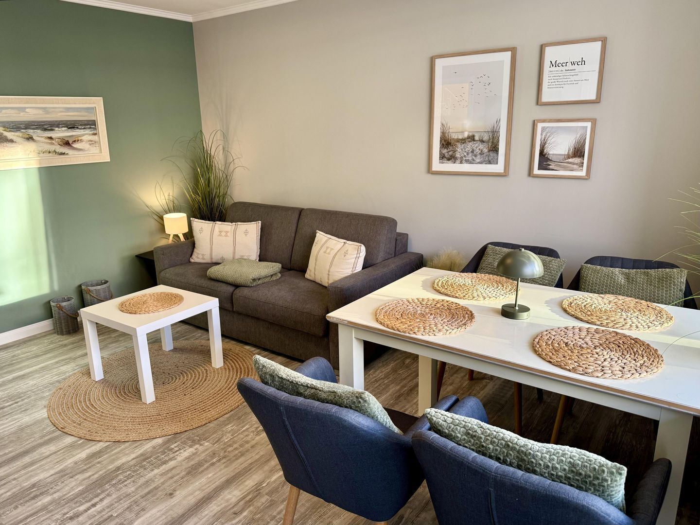 Un salon moderne avec un canapé gris, une table basse blanche et des chaises bleues. On trouve des sets de table en fibres naturelles sur la table et une lampe sur une petite table d’appoint.