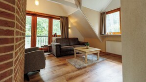 Un vaste espace de vie de style loft, doté d’une grande fenêtre, d’un canapé en cuir marron, d’une table basse en bois et d’un mur en briques.