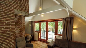 Une pièce avec un mur en briques, un plancher en bois, deux canapés, une table et une porte-fenêtre coulissante donnant sur un espace extérieur.