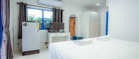 A hotel room with a bed, a desk, a wardrobe, and an air conditioning unit.