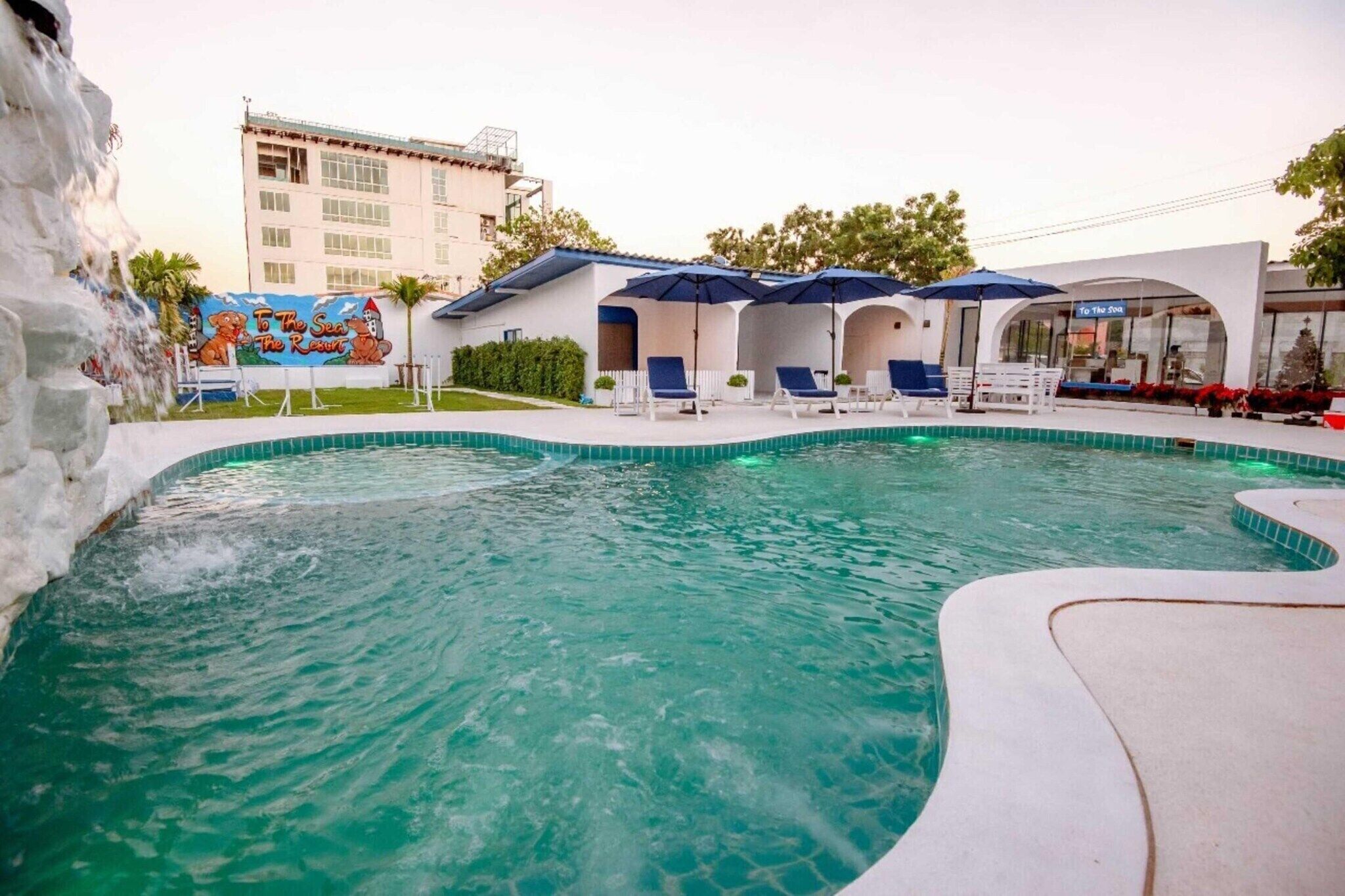 A swimming pool with lounge chairs and umbrellas, a mural, and a building in the background.