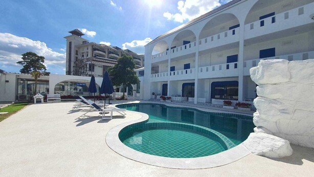 A swimming pool with a white rock feature, a multi-story building with balconies, and a clear blue sky.