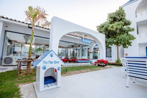 A pet-friendly hotel with a dog house labeled "To The Sea," a palm tree, and a bench.