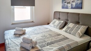 A neatly made bed with rolled towels, a window with a blind, and a painting of sailboats on the wall. - 2 bedroom awesome apartment in Vir (Vir)