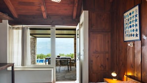 A bedroom with a wooden ceiling, a bed, a nightstand with a lamp, and a view of a patio with a table and chairs. - Pet friendly home in Postira (Postira)