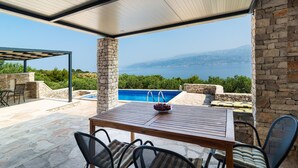A covered outdoor area with a pool, stone pillars, and a table with chairs. - Pet friendly home in Postira (Postira)