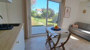 A modern kitchen with a sliding glass door leading to a balcony, a dining table with chairs, and a grey sofa with patterned cushions. - Cozy studio in a peaceful garden (Villenave-d'Ornon)