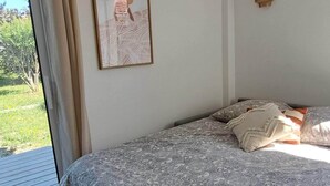 A bedroom with a bed, a window with curtains, a wall-mounted air conditioner, and a framed picture. - Cozy studio in a peaceful garden (Villenave-d'Ornon)