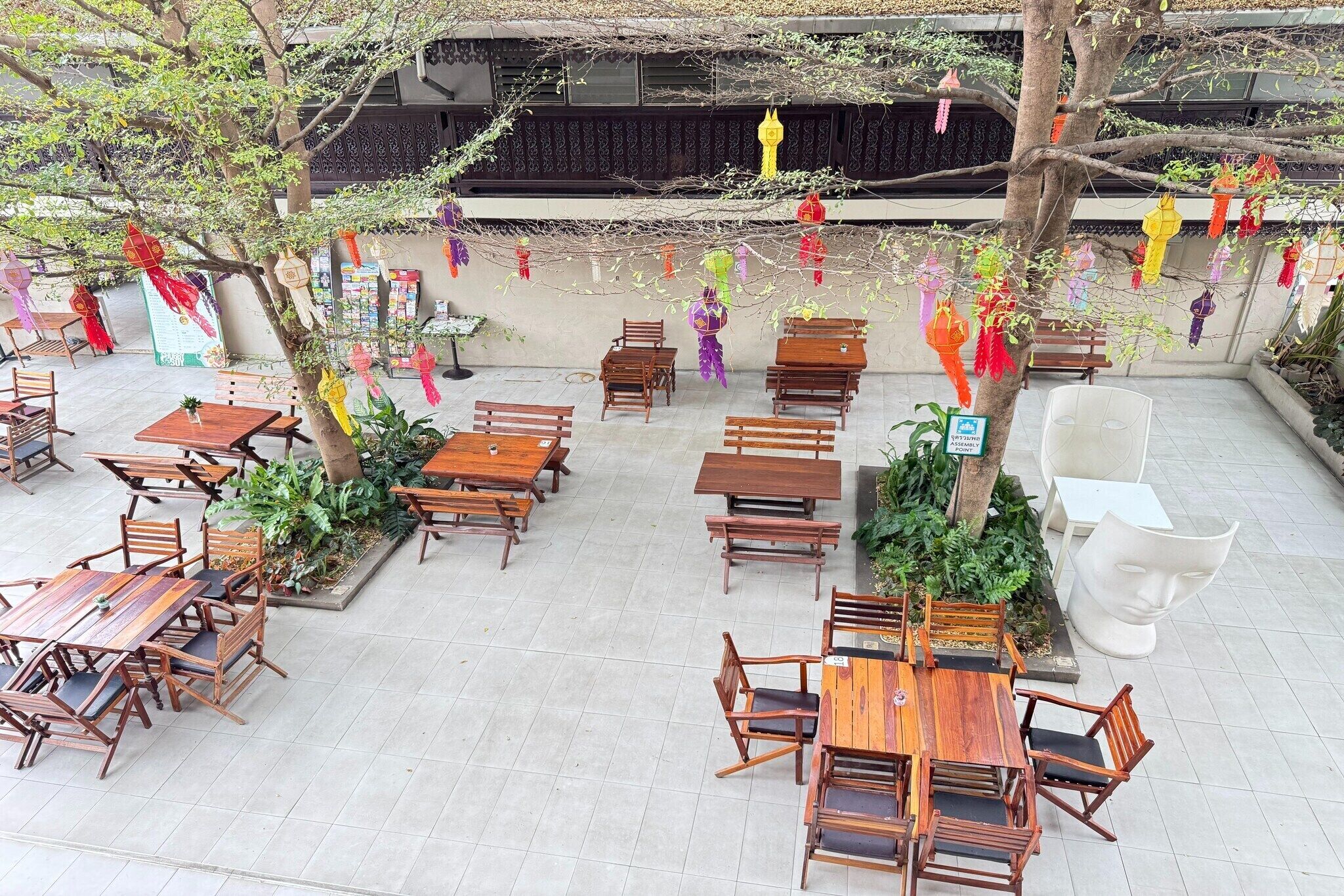 An outdoor dining area with wooden tables and chairs, surrounded by plants and trees.