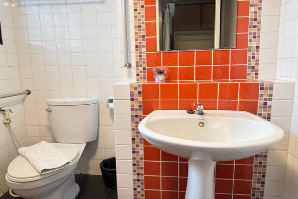 A bathroom with a white toilet, a white sink, and a tiled wall with a mix of white and multicolored tiles.
