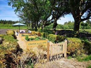 Een tuin met verhoogde borders, een houten poort en een bank onder een parasol.