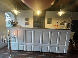 Een keuken met een witte bar, hangende hanglampen, een raam met uitzicht en een vloer van baksteen.