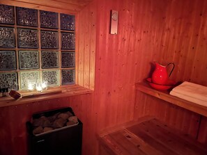 Interieur van een houten hutje met een raam, een rode waterkoker, een plank met een handdoek en een prullenbak.