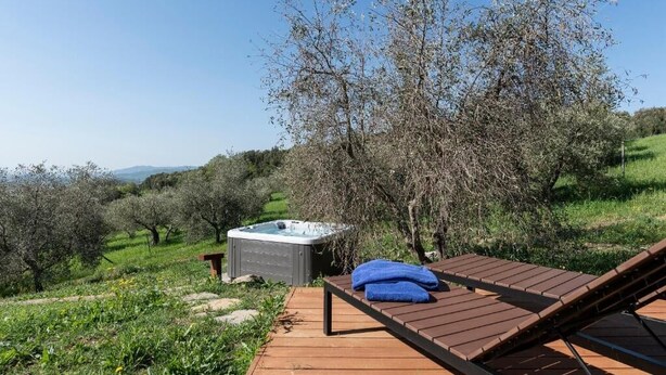 A wooden deck with a hot tub and a lounge chair, surrounded by greenery and trees. - Casa Gialla (Gavorrano)