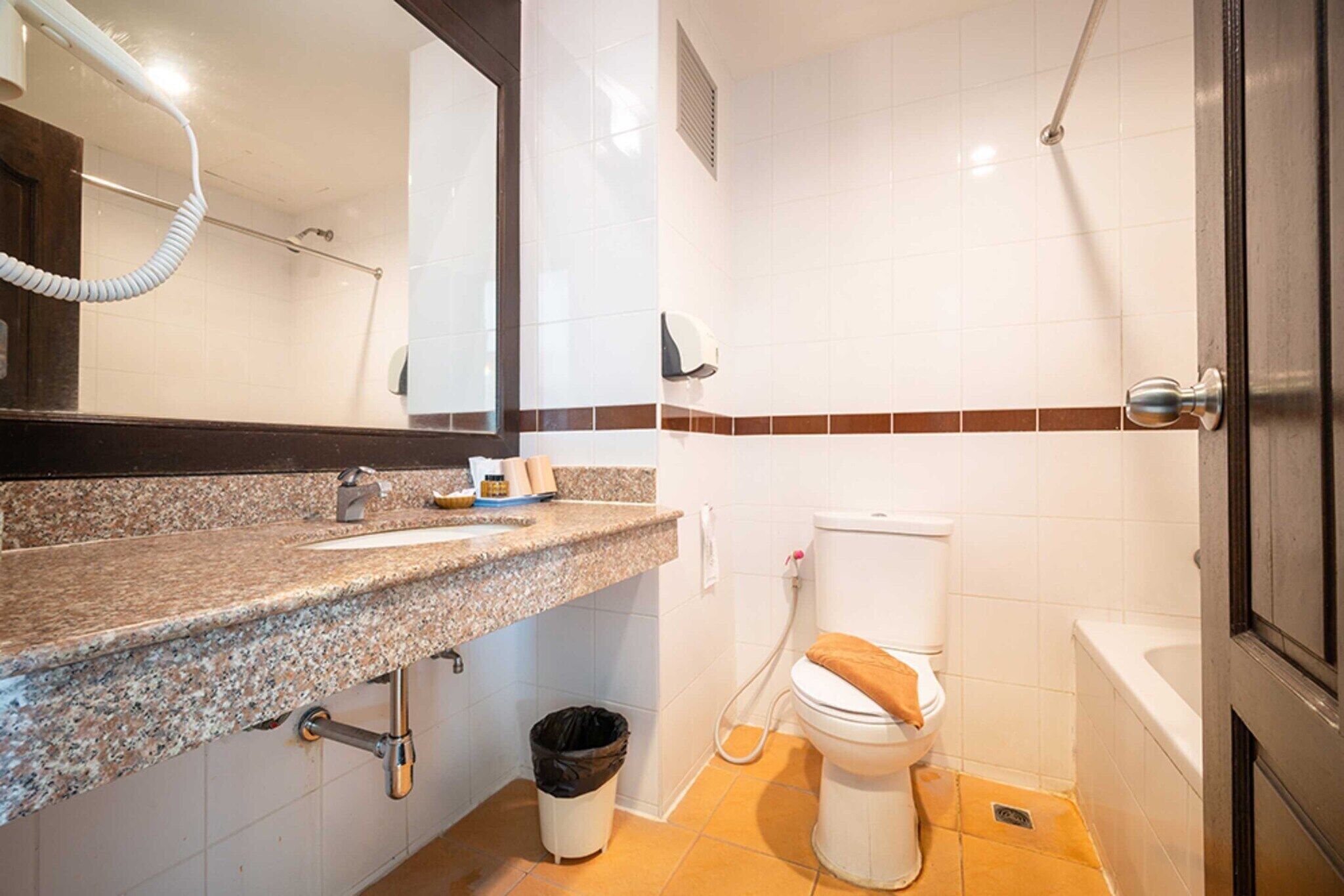 Un baño con encimera de granito, inodoro, ducha y cubo de basura.