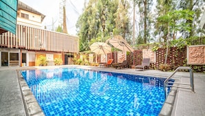 A swimming pool with tiled blue water, surrounded by a wooden fence, and adjacent to a building with a balcony.