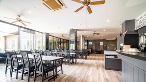 A spacious restaurant with high ceilings, ceiling fans, and large windows. Tables and chairs are arranged for dining.