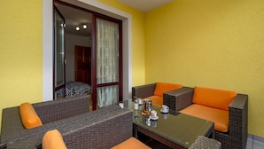 A dining area with wicker furniture and orange cushions, a glass table with cups and a pitcher, and a view through a glass door. - Cozy apartment in Vrbovsko with sauna (Vrbovsko)