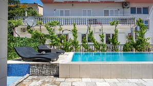 A swimming pool with lounge chairs and a stone wall. - Beautiful apartment in Sibenik (Sibenik)