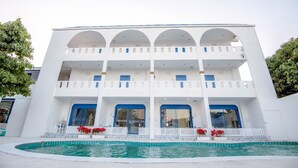 Un edificio blanco con piscina delantera, con balcones y puertas azules.
