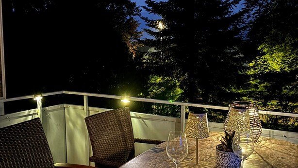 Un espacio de comedor al aire libre con sillas de mimbre y una mesa, bajo un cielo nocturno con una luna visible.