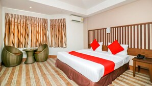 Une chambre d’hôtel avec un grand lit, deux oreillers rouges, une tête de lit en bois, une petite table avec des chaises et un climatiseur fixé au mur.