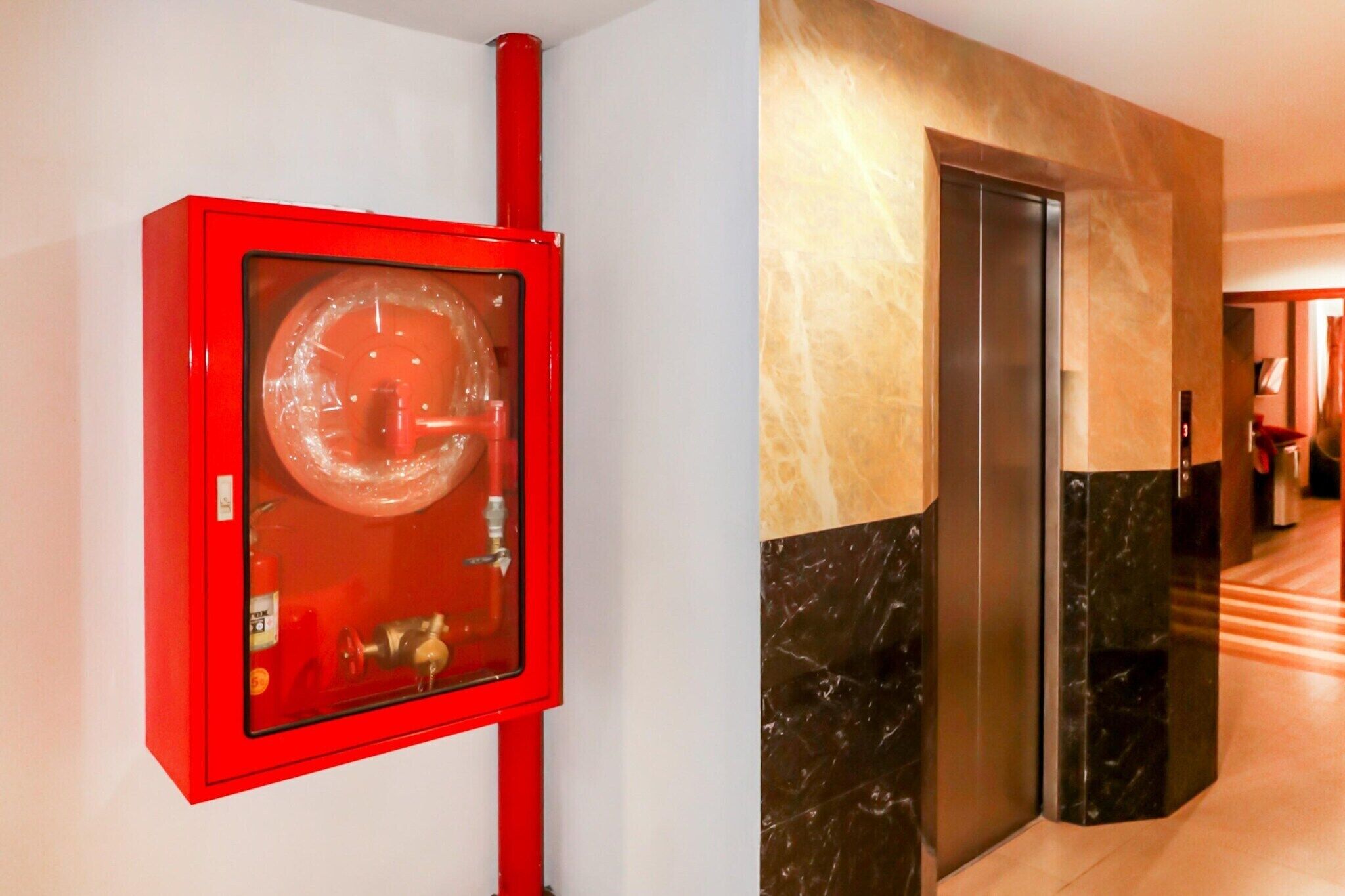 A red emergency equipment box and a marble elevator in a hallway.