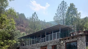 A stone building with a balcony, a small patio with chairs, and a mountainous backdrop. - Kafal Resort (Kosiyakutoli)