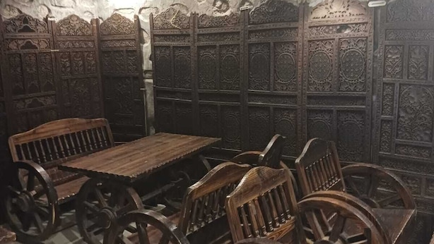 A room with a rustic wooden table and chairs, stone walls with intricate carvings, and hanging lamps. - Kafal Resort (Kosiyakutoli)
