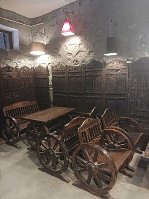 A room with a rustic wooden table and chairs, stone walls with intricate carvings, and hanging lamps.