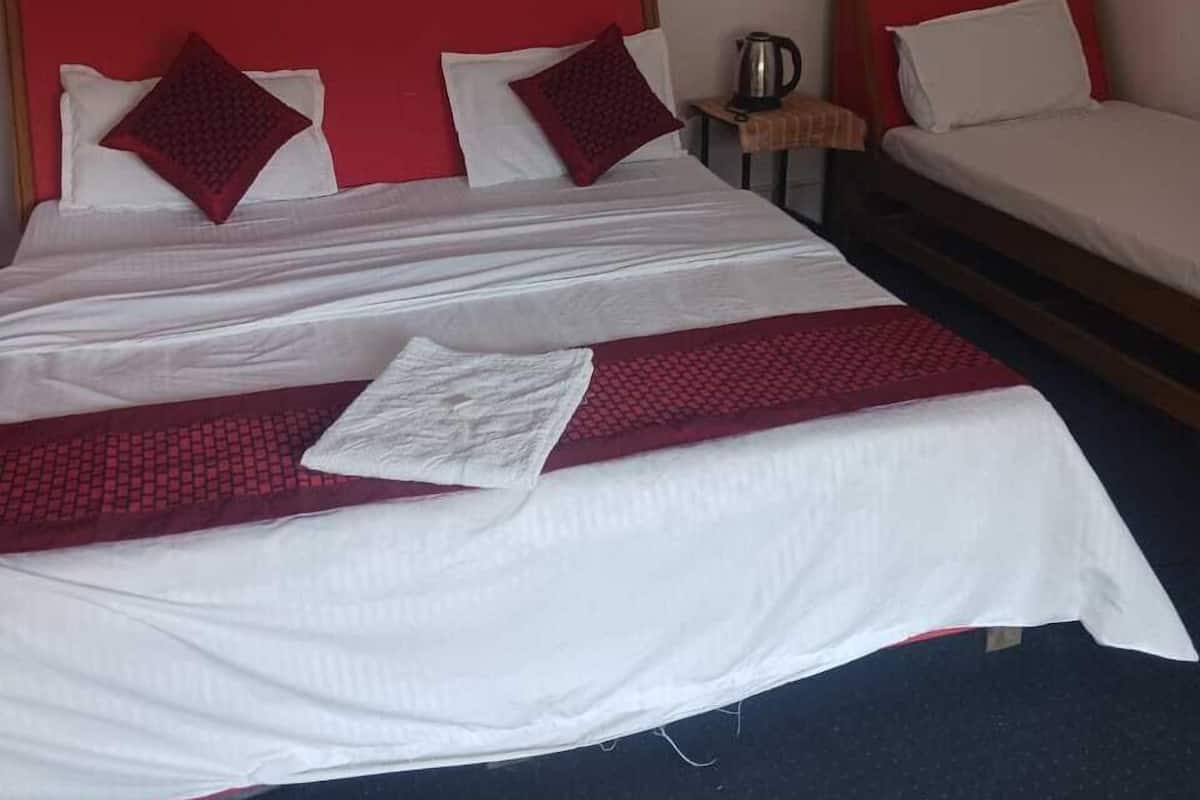 A hotel room with two beds, each with red headboards and white bedding. There is a small table with a kettle and a picture on the wall.