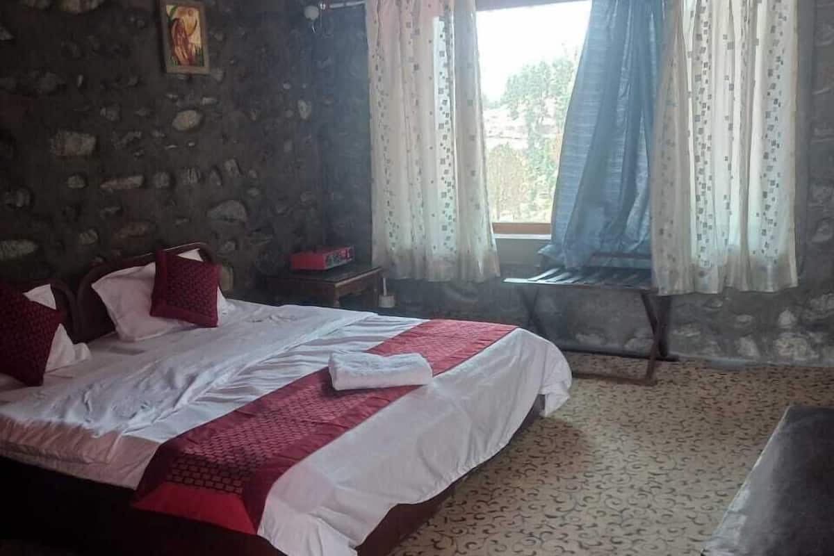 A room with a bed, a wooden chair, a small table, and a window with curtains.