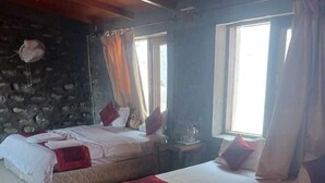 A room with two beds, a stone wall, and a window with curtains. - Kafal Resort (Kosiyakutoli)