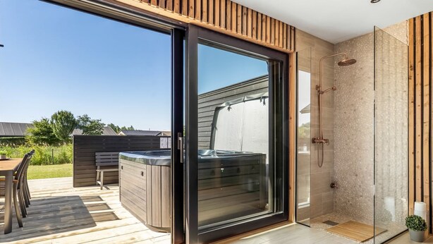 A modern bathroom with a glass shower enclosure, a hot tub, and a deck area with outdoor furniture. - "Merve" - 250m from the sea by Interhome (Odder)