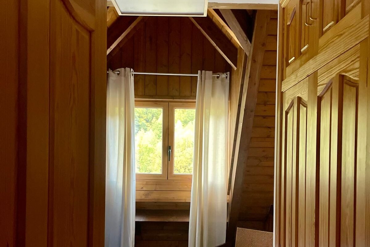 Houten cabin inrichting met slaapkamer op zolder, een klein eetgedeelte en uitzicht op groen.