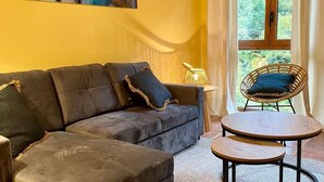 A living room with a sofa, a small table, a wicker chair, and a painting on the wall. - Apartamentos Snö Escarrilla (Sallent de Gallego)