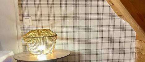 A cozy room with a plaid wallpaper, a small round table with a woven lamp, and a woven rug on the floor.