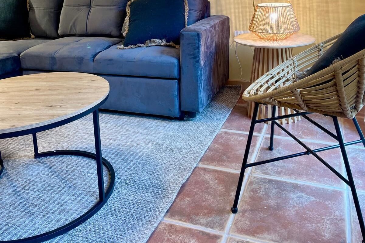 Un salon avec un canapé, une table basse ronde, un fauteuil en osier et un tableau accroché au mur.