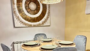 A dining area with a round table, grey upholstered chairs, and a decorative wall piece above. - Apartamentos Snö Escarrilla (Sallent de Gallego)