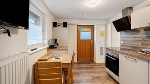 Una cocina compacta con una mesa de comedor, sillas, horno empotrado, microondas y ventana con persianas.