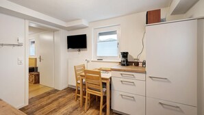Una cocina compacta con una mesa de comedor, sillas, un televisor sobre la ventana y un refrigerador.