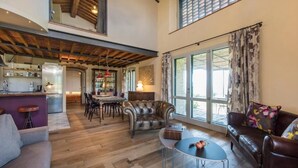 A spacious living area with a wooden floor, leather sofas, a dining table, and a kitchen in the background. - Oak (Gavorrano)
