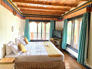 A bedroom with a bed, a TV, and a balcony with curtains. - Sinchula Villa (Paro)