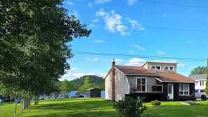 A house with a stone wall in the foreground, a grassy yard, and a clear blue sky with clouds. - The Tidehouse, Relax with the whole family at this peaceful place to stay. (Laurenceton)