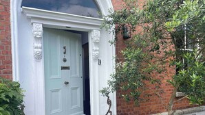 A white door with decorative moldings, a small tree in front, and a brick wall.