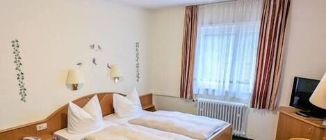 Habitación de hotel con cama, escritorio, silla, televisor y ventana con cortinas.