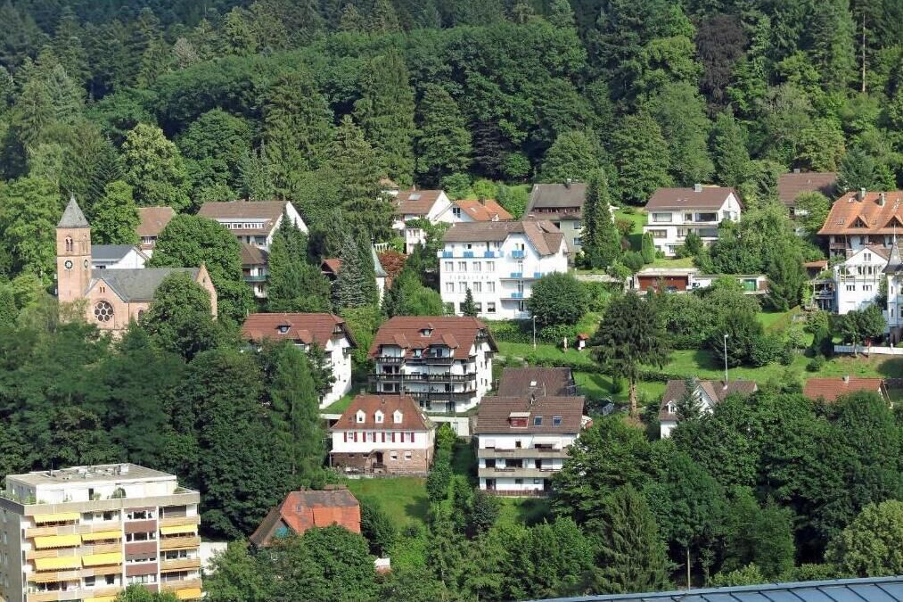 A residential area with a mix of single and multi-story houses, surrounded by dense greenery and a church with a bell tower.